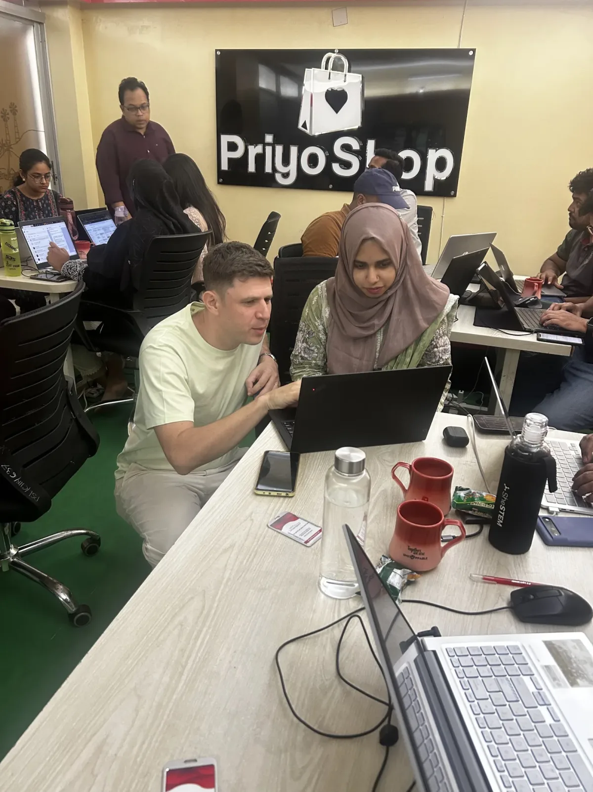 Alex Miller pair-programming with a participant during a PriyoShop workshop in Dhaka