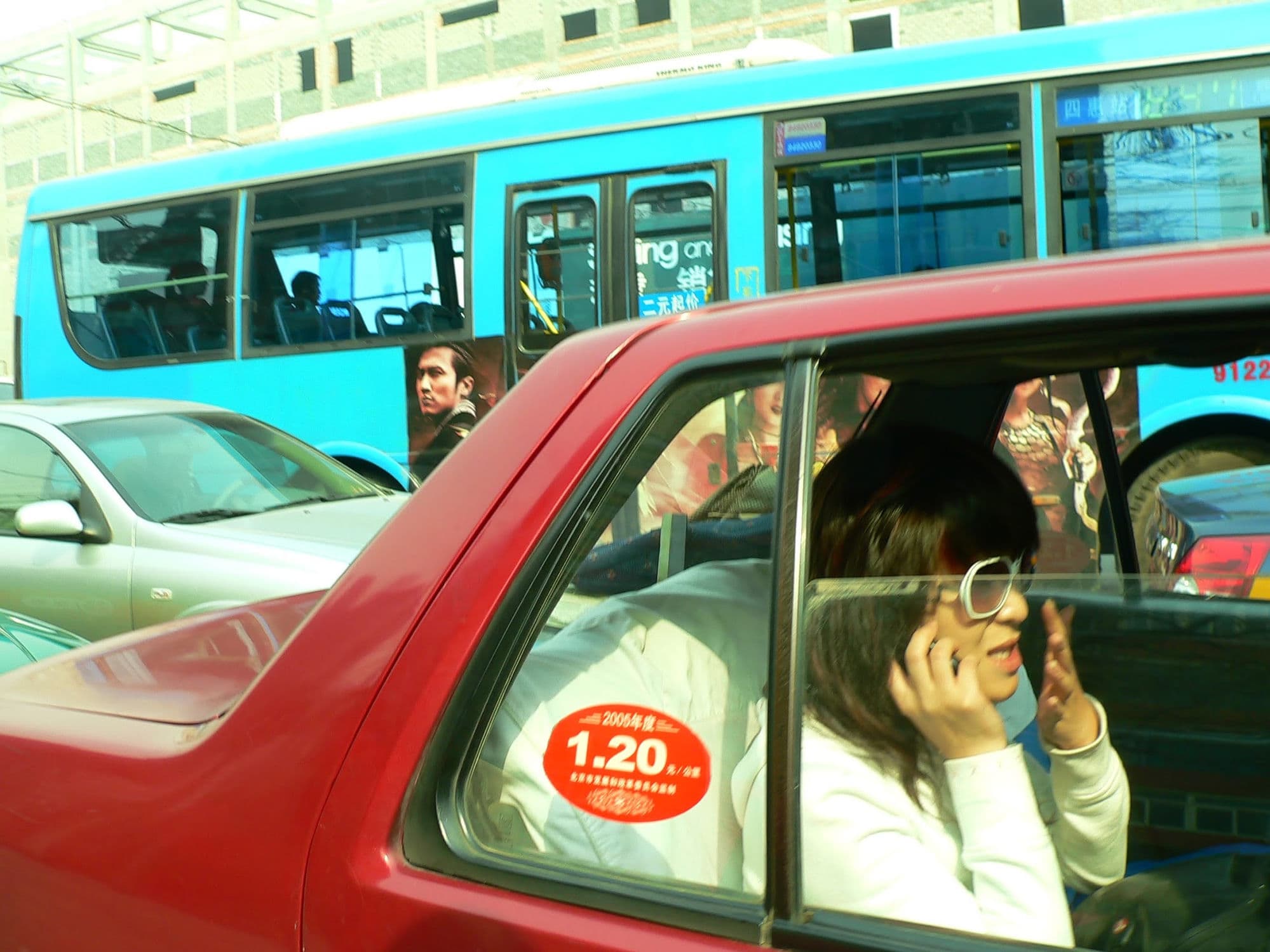 A red Beijing taxi beside a blue city bus, a woman on her phone in the back seat, Beijing 2005