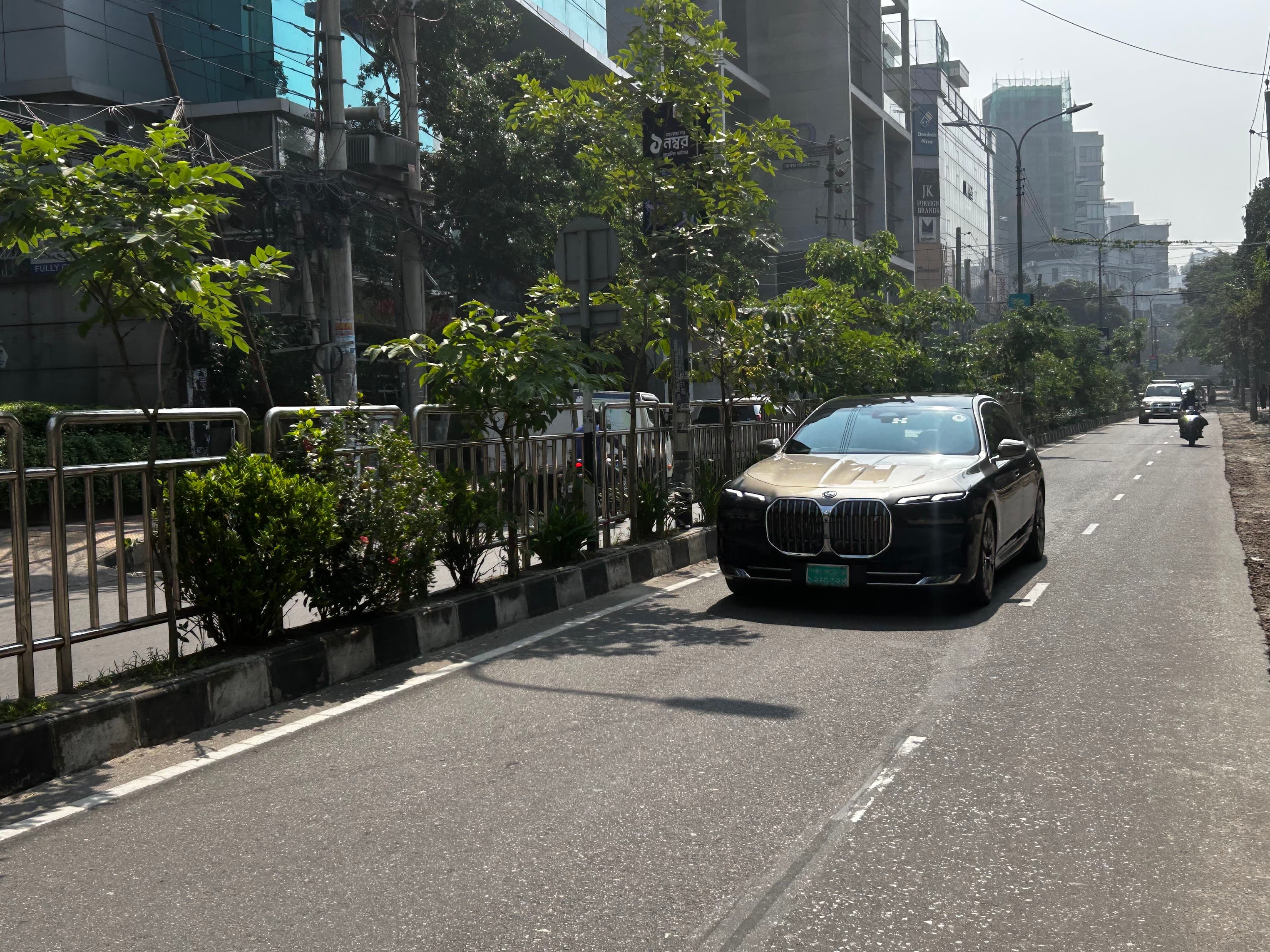 A black electric BMW 7 Series on a tree-lined avenue in Dhaka, 2026