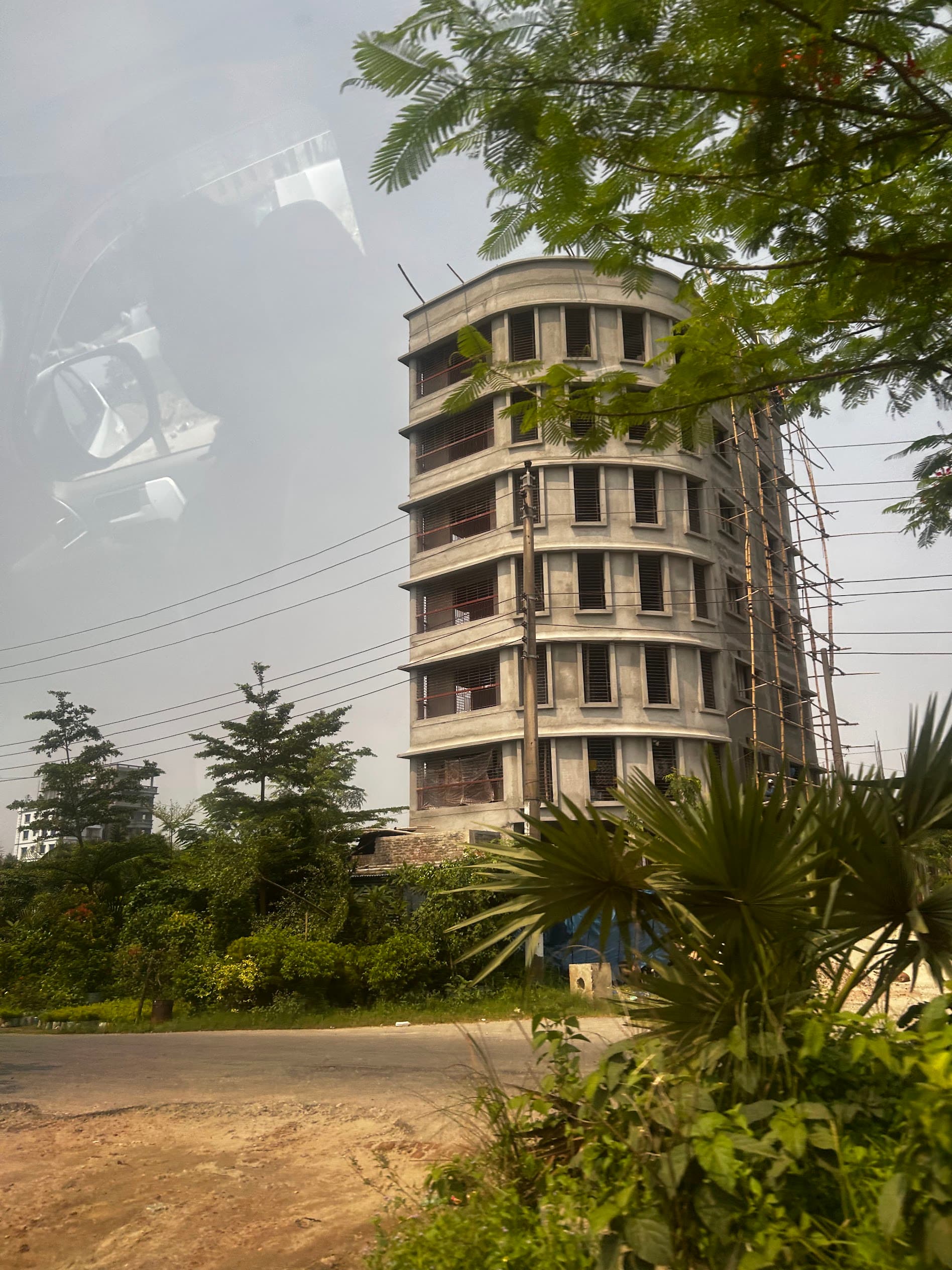 A multi-storey concrete building under construction with bamboo scaffolding, Dhaka 2026