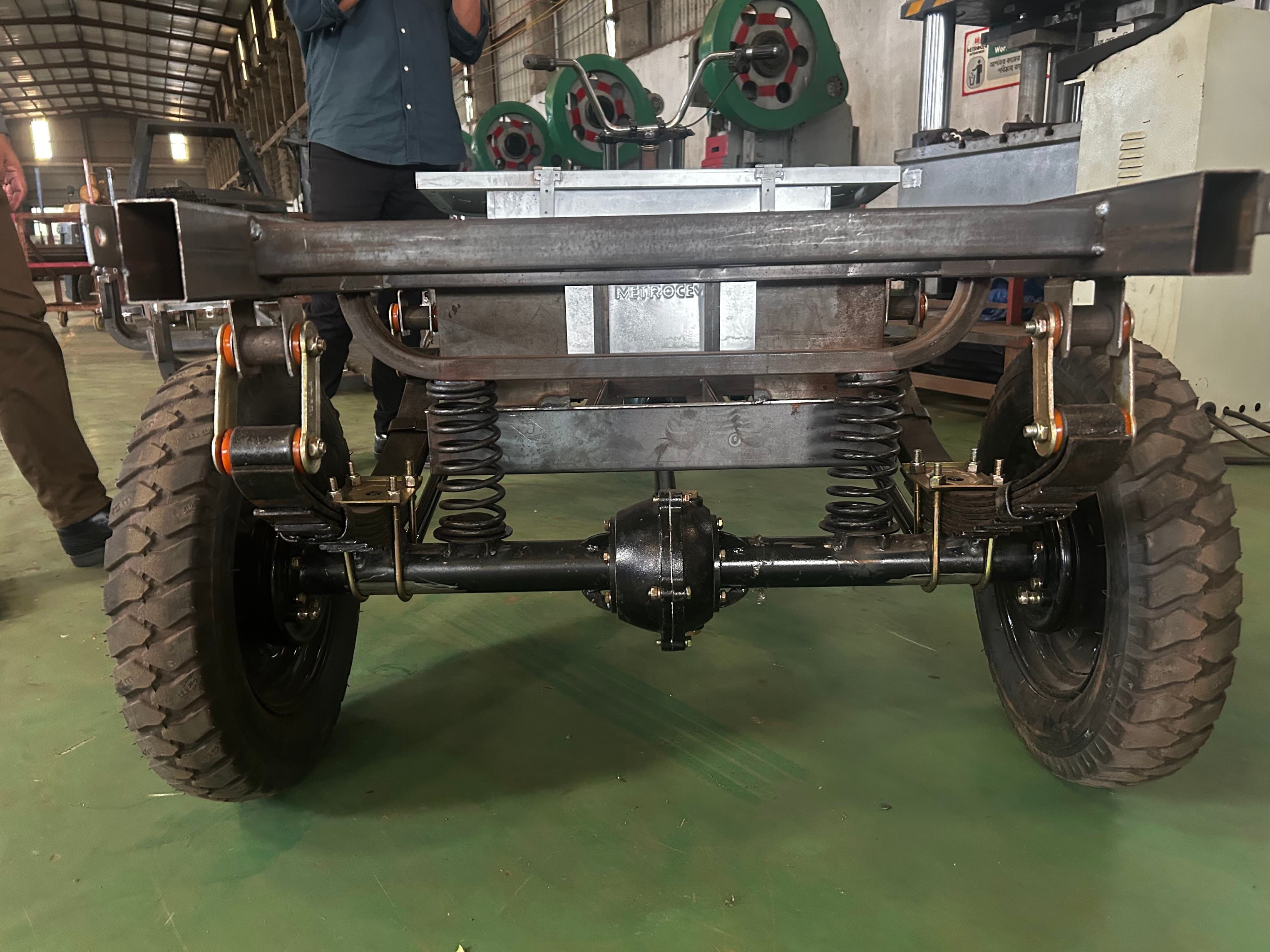 The underside of an electric-vehicle chassis on a workshop floor, Bangladesh 2026